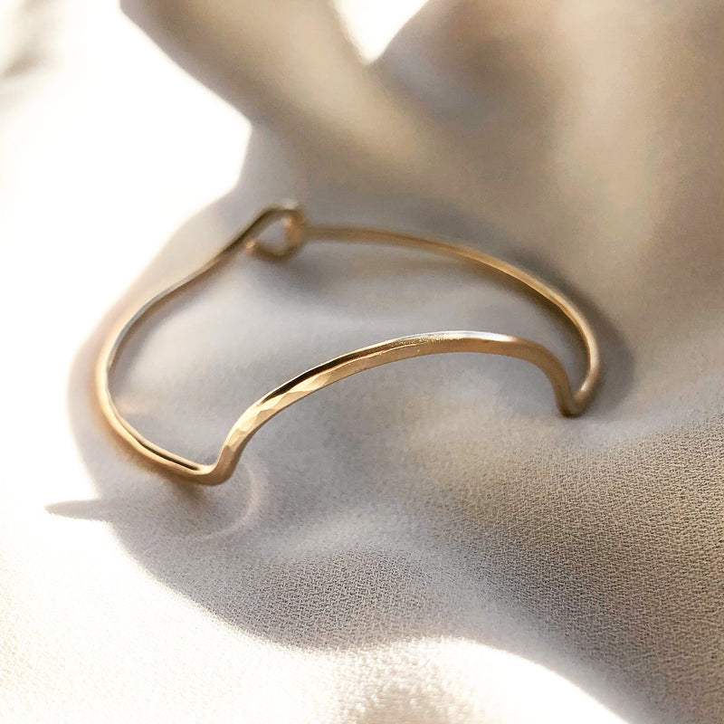 handmade gold bangle bracelet with crescent moon detail, laying in the sunlight 