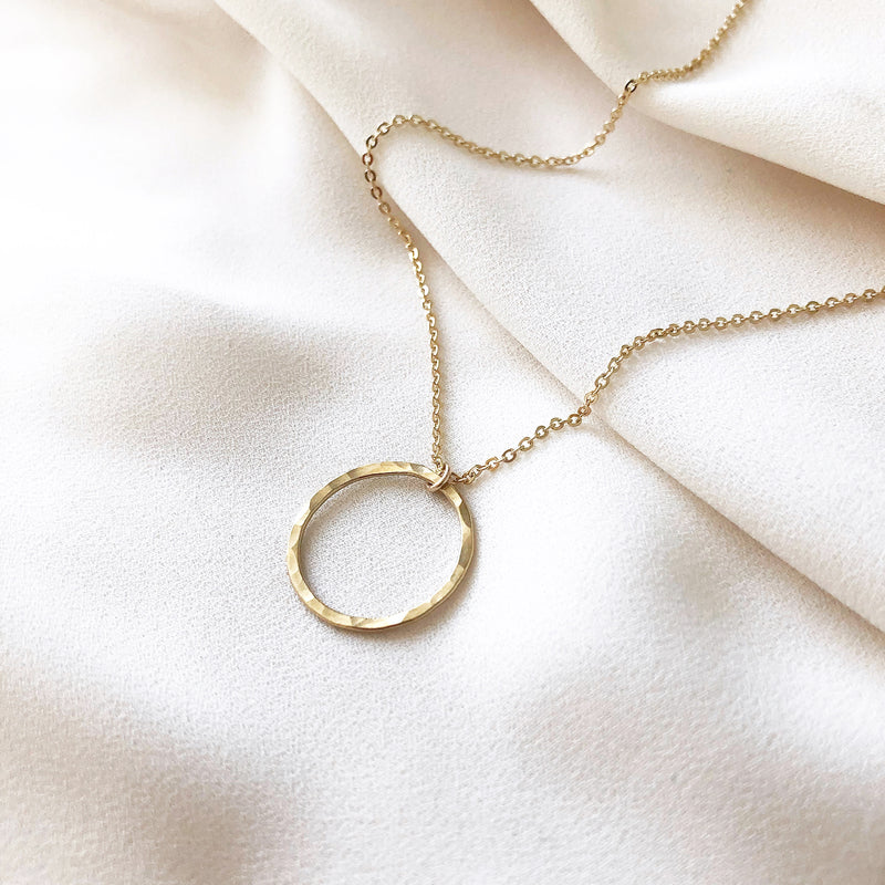 handmade gold circle necklace, on a gold filled chain, laying on a white fabric background 