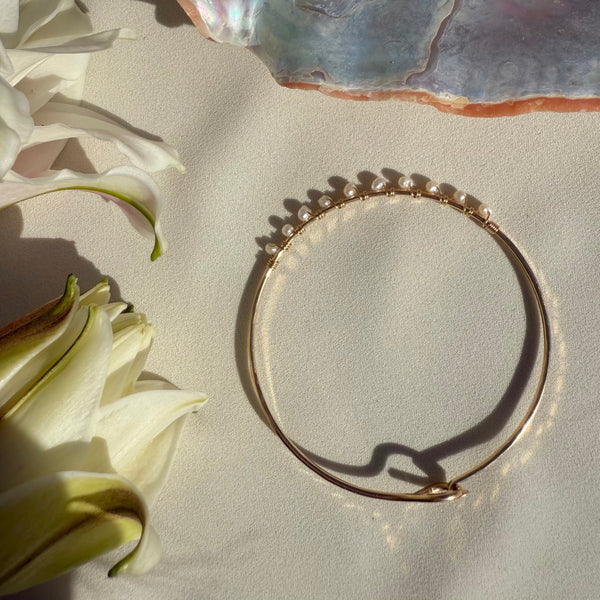 Gold bracelet on a textured surface with flowers and a shell in the background
