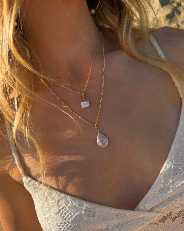 Close-up of a necklace with a pendant on a person wearing a lace top.