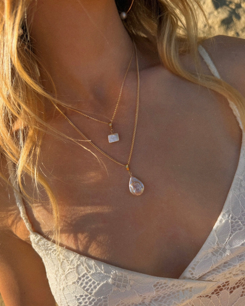 Close-up of a necklace with a pendant on a person wearing a lace top.