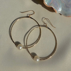Gold hoop earrings with pearls on a light background