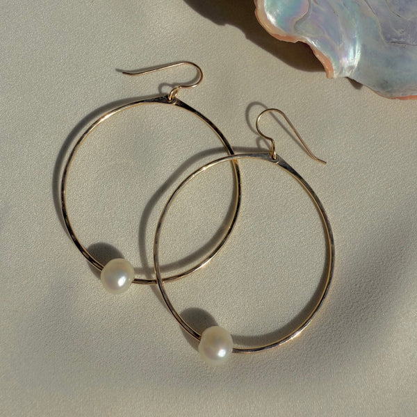 Gold hoop earrings with pearls on a light background