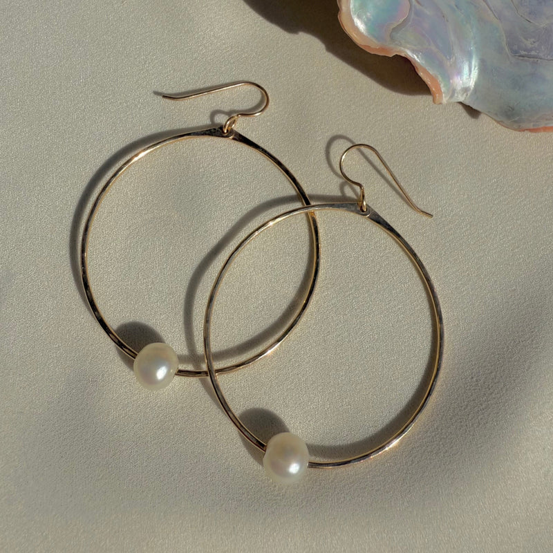Gold hoop earrings with pearls on a light background