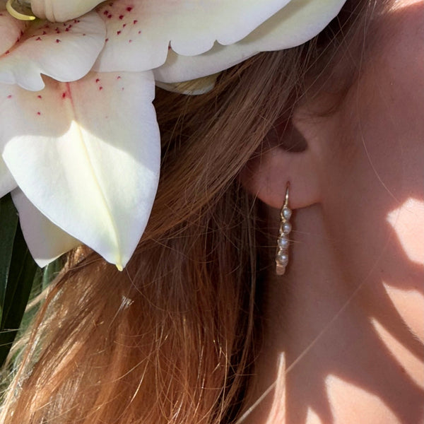 Close-up of a person wearing pearl earrings with a white flower in the background.