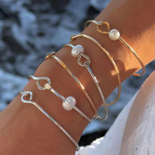 Close-up of a wrist wearing multiple pearl-embellished bracelets against a rocky background.