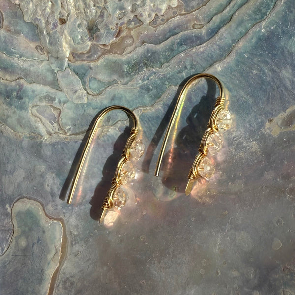 Gold earrings with herkimer diamond stones on a textured stone surface