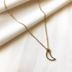 gold, crescent moon necklace meant to signify inner strength and wisdom,  laying on a white fabric background 