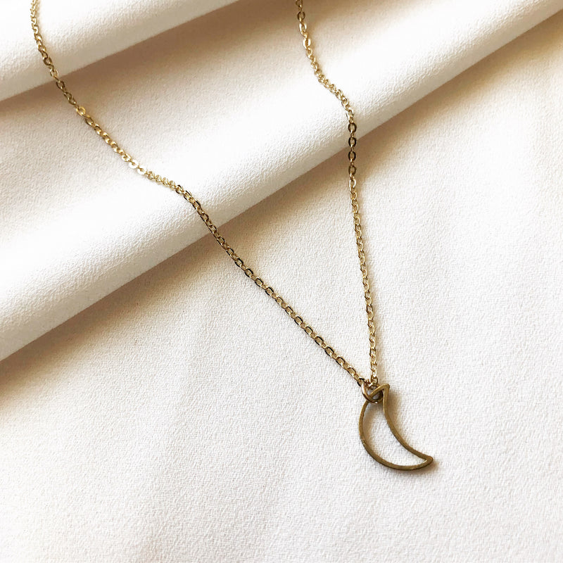gold, crescent moon necklace meant to signify inner strength and wisdom,  laying on a white fabric background 