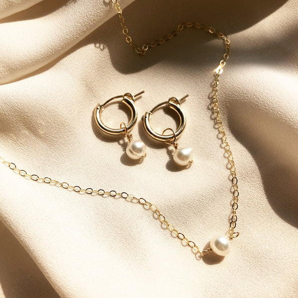 gold hoop, pearl earrings and a matching gold pearl necklace, placed in the sunlight on a white fabric