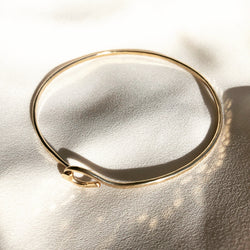 14k gold filled, handmade bangle, placed on a white fabric background. 