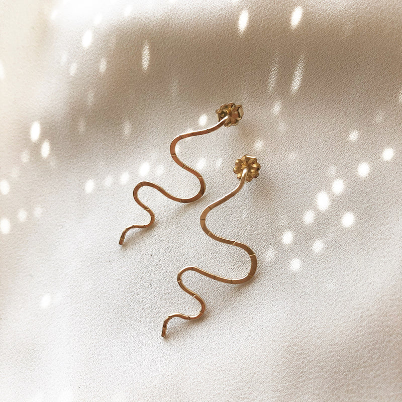 handmade snake earrings, which a studs placed on a white fabric 
