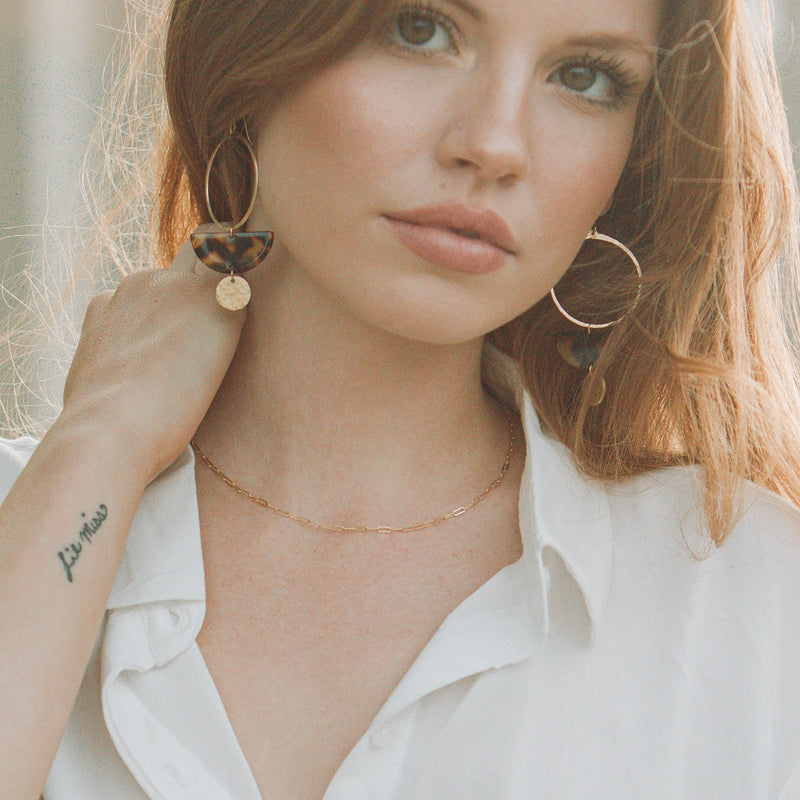Model wearing white shirt and handmade earrings, acrylic tortoise shell earrings with gold disc detail, and gold chain necklace 