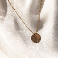 handmade, gold coin necklace on a gold chain, laying in the sunlight 