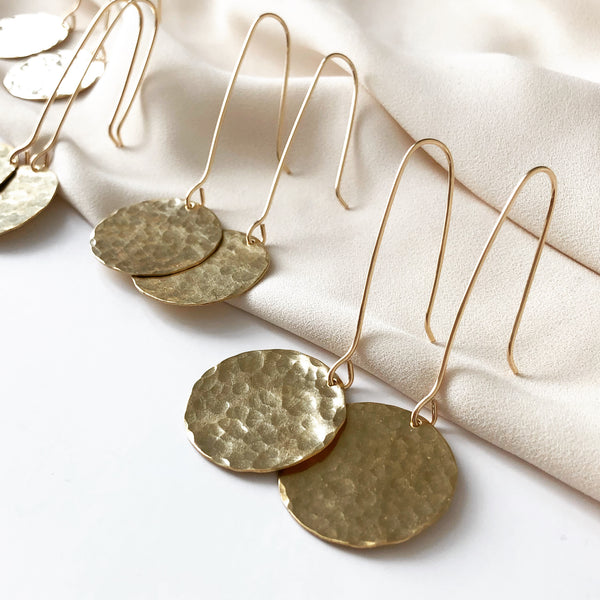 handmade earrings, large gold disc earrings which resemble a full moon, resting on a white fabric 