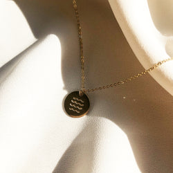 gold disc necklace hand stamped with  ocean waves, laying in the sunlight 